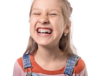 Portrait of little girl with orthodontics appliance isolated on white background.